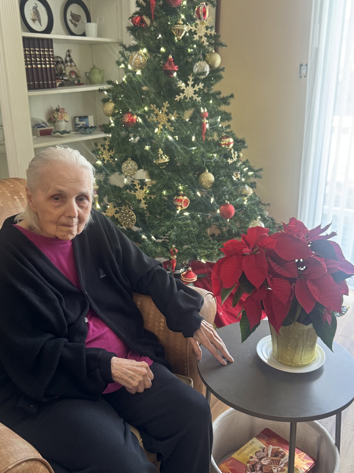 Resident at Christmas with a poinsettia by the tree